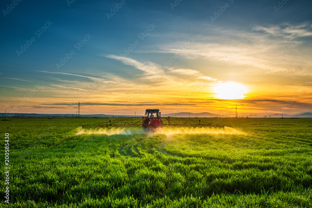 Obraz premium Farming tractor plowing and spraying on field