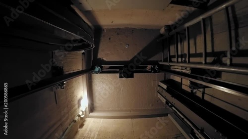 The cabin moves up in an elevator shaft. The view is directed downwards. The camera is moving. The lights in the shaft give the ride its own rhythm.
