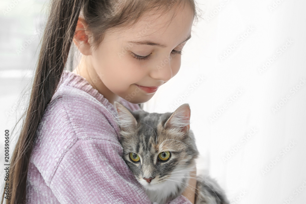Cute little girl with cat near window at home