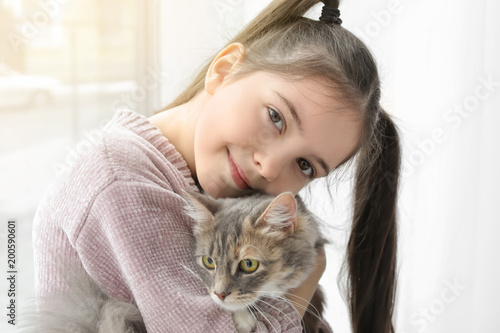 Cute little girl with cat near window at home
