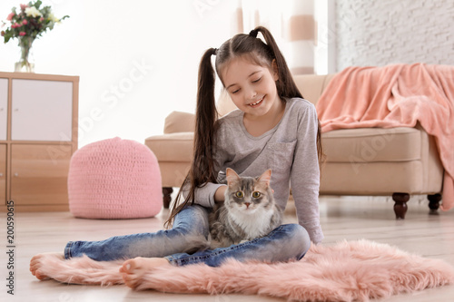 Cute little girl with cat sitting on floor at home