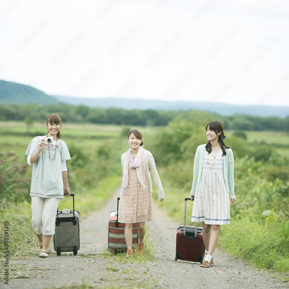 旅行鞄を持ち一本道を歩く3人の女性 Stock Photo Adobe Stock