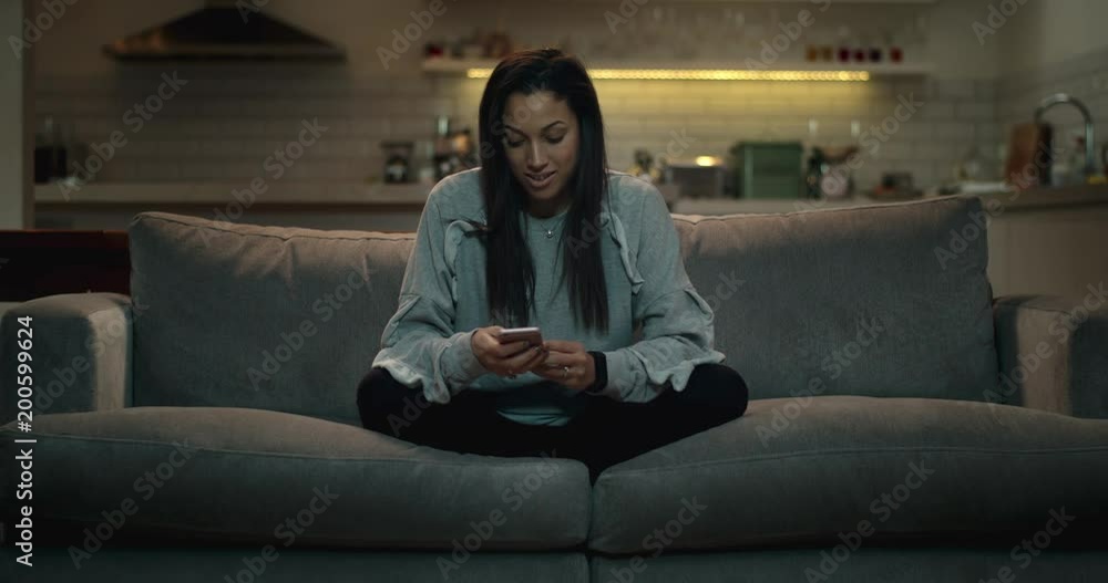Girl sitting crossed legged on a sofa using her smartphone to chat with her friends online. Girl sitting crossed legged on a sofa using her smartphone to chat with her friends online.