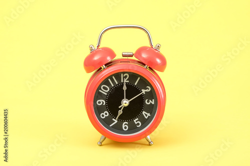Red vintage alarm clock on yellow background.