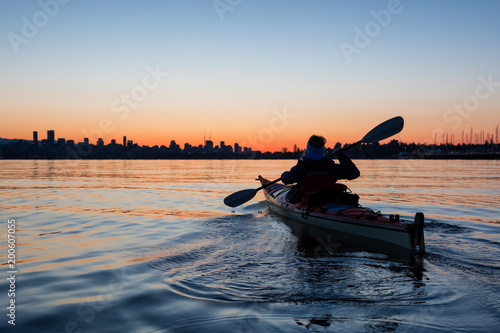 Adventurous Girl Sea Kayaking during a vibrant winter sunrise with City Skyline in Background. Taken in Downtown Vancouver, British Columbia, Canada.