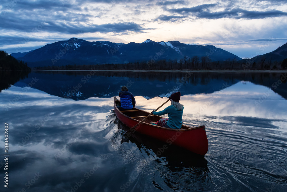 Adventurous people on a wooden canoe are enjoying the beautiful Canadian Mountain Landscape during a vibrant sunset. Taken in Harrison River, East of Vancouver, British Columbia, Canada.