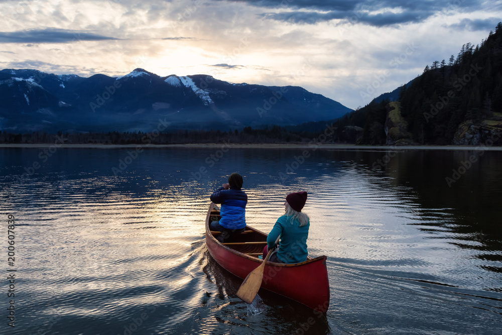 Adventurous people on a wooden canoe are enjoying the beautiful Canadian Mountain Landscape during a vibrant sunset. Taken in Harrison River, East of Vancouver, British Columbia, Canada. Adventurous people on a wooden canoe are enjoying the beautiful Canadian Mountain Landscape during a vibrant sunset. Taken in Harrison River, East of Vancouver, British Columbia, Canada.