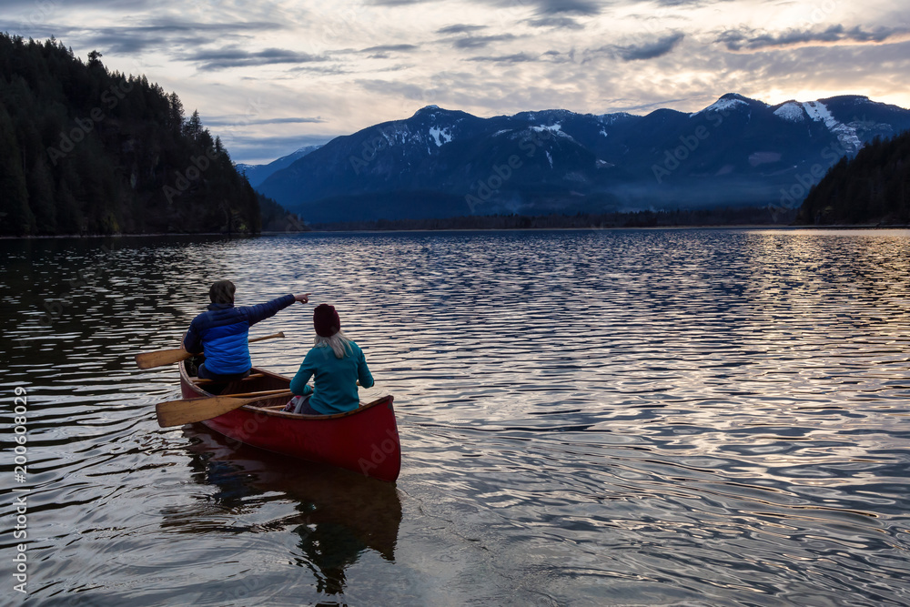 Adventurous people on a wooden canoe are enjoying the beautiful Canadian Mountain Landscape during a vibrant sunset. Taken in Harrison River, East of Vancouver, British Columbia, Canada.