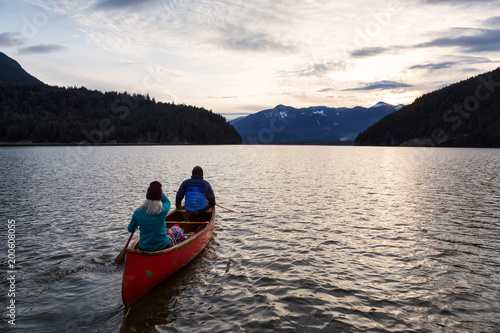 Adventurous people on a wooden canoe are enjoying the beautiful Canadian Mountain Landscape during a vibrant sunset. Taken in Harrison River  East of Vancouver  British Columbia  Canada.