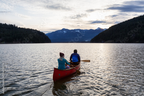 Adventurous people on a wooden canoe are enjoying the beautiful Canadian Mountain Landscape during a vibrant sunset. Taken in Harrison River  East of Vancouver  British Columbia  Canada.