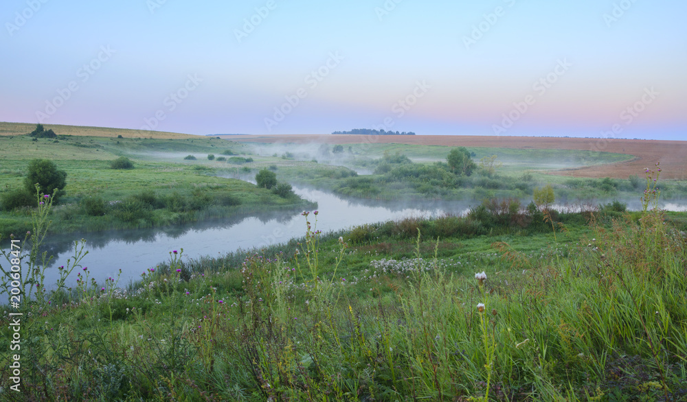 Summer landscape.Green meadows and river at sunrise.Fog over the water. 
