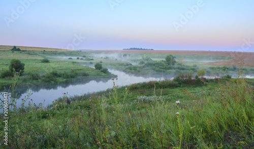 Summer landscape.Green meadows and river at sunrise.Fog over the water. 