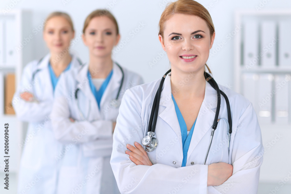 Beautiful female medical doctor standing at hospital in front of medical group. Physician is ready to help patients. Medicine and health care concept Beautiful female medical doctor standing at hospital in front of medical group. Physician is ready to help patients. Medicine and health care concept