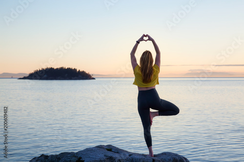 Young woman practicing yoga on a rocky island during a vibrant sunset. Taken in Whytecliff Park  Horseshoe Bay  West Vancouver  British Columbia  Canada.