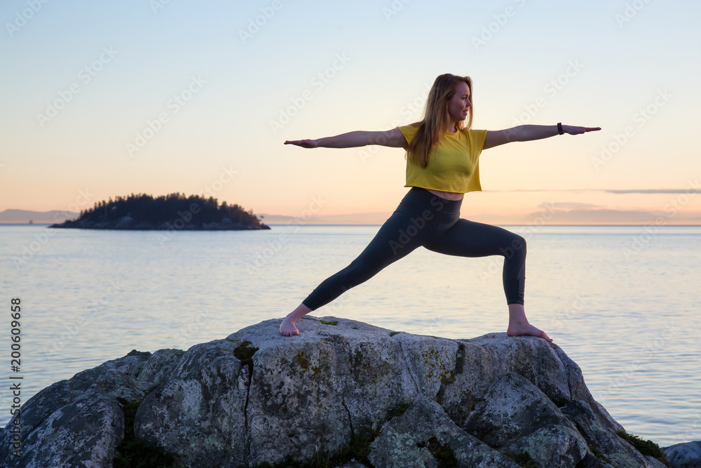 Young woman practicing yoga on a rocky island during a vibrant sunset. Taken in Whytecliff Park, Horseshoe Bay, West Vancouver, British Columbia, Canada. Young woman practicing yoga on a rocky island during a vibrant sunset. Taken in Whytecliff Park, Horseshoe Bay, West Vancouver, British Columbia, Canada.