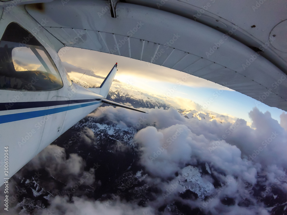 Fototapeta premium Small airplane flying over the Canadian Mountain Landscape during a vibrant sunset. Taken near Squamish, North of Vancouver, British Columbia, Canada.