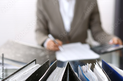 Binders with papers are waiting to be processed with businesswoman or secretary back in blur