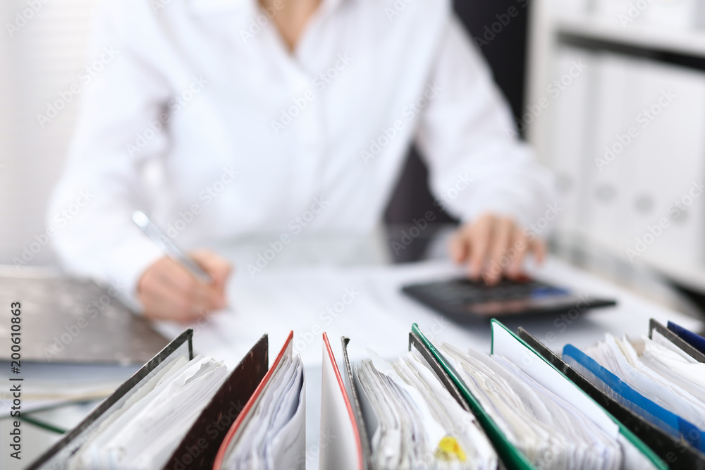 Binders with papers are waiting to be processed with businesswoman or secretary back in blur Binders with papers are waiting to be processed with businesswoman or secretary back in blur