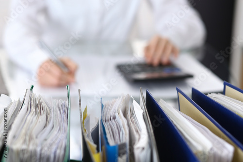 Binders with papers are waiting to be processed with businesswoman or secretary back in blur
