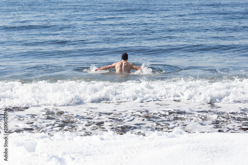 Man swimming in the cold ocean in winter. Taken in Ambleside Park, West Vancouver, British Columbia, Canada.