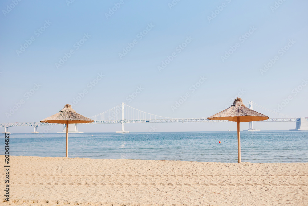 Sand beach. Beach straw umbrellas against the background of the blue sea and the sky.