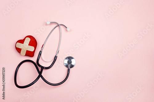 Stethoscope and heart with adhesive plaster on pink background. Flat lay and copy space.