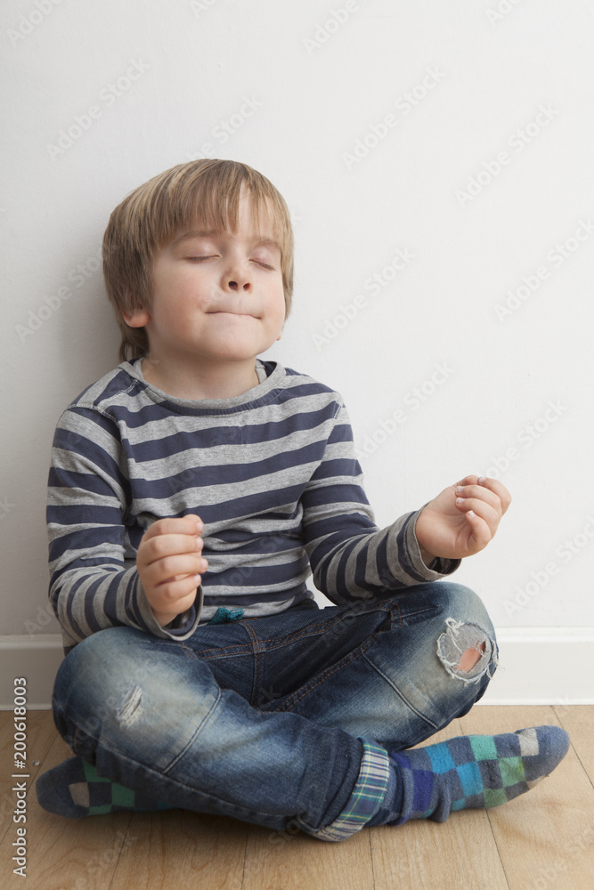 Niño (5 años) sentado en el suelo meditando con los ojos cerrados y boca cerrada. Niño (5 años) sentado en el suelo meditando con los ojos cerrados y boca cerrada.