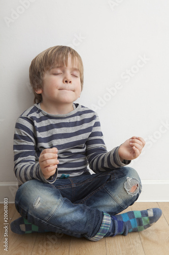 Niño (5 años) sentado en el suelo meditando con los ojos cerrados y boca cerrada. photo