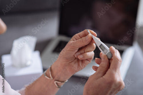 Close up of a thermometer in hands of an unhealthy senior woman