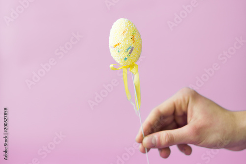 Man holding a yellow easter egg on a stick on a pink background photo