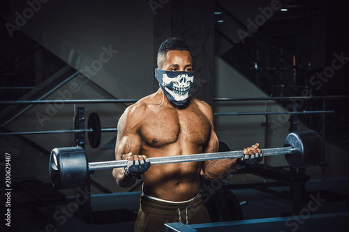 muscular young african american man in mask lifting barbell on biceps. Exercise for biceps with barbell. black man in gym