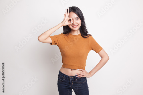 Beautiful young Asian woman show OK sign over her eye.