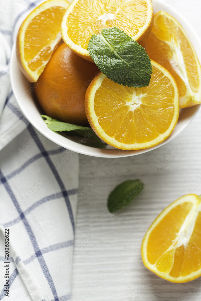 Fototapeta premium oranges in a white cup and mint leaves on a white wooden background closeup.