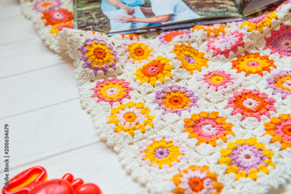 Fototapeta premium Pregnancy and preparation for childbirth. Motley handmade knitted baby blanket, rattles, photo album with a photo of pregnancy and opend notebook with empty blanks for text. Selective focus.