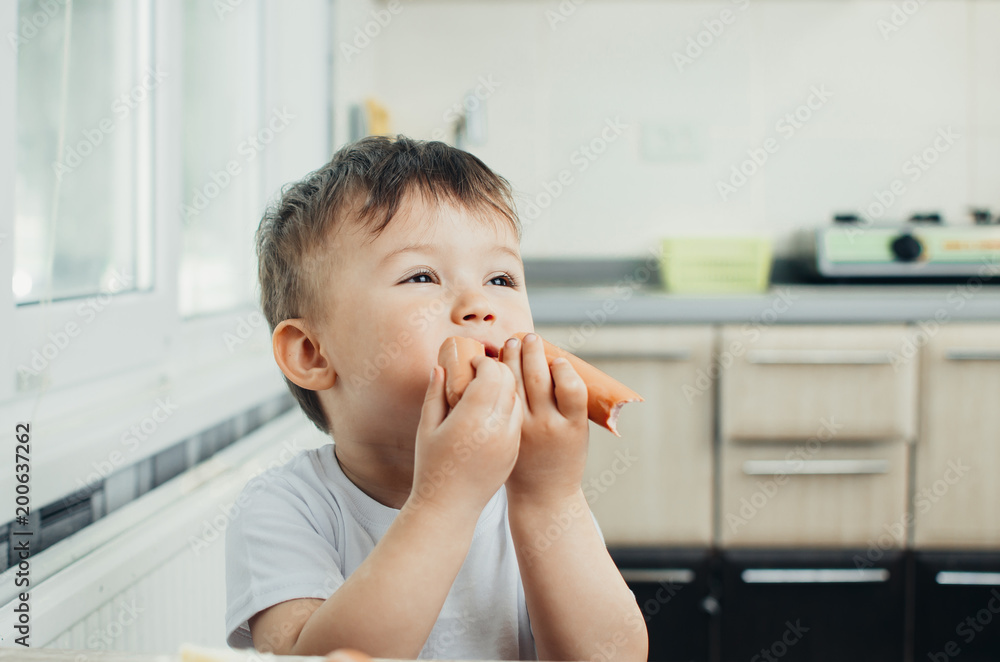 handsome boy shaggy and shkod eats sausage in the kitchen in a white t-shirt in the afternoon handsome boy shaggy and shkod eats sausage in the kitchen in a white t-shirt in the afternoon