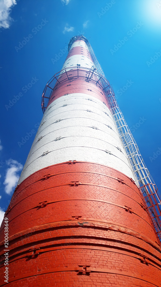 Red-white chimney of a large plant. Bottom view. On the blue sky background.