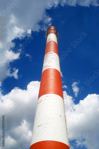 Red-white chimney of a large plant. Bottom view. On the blue sky background.