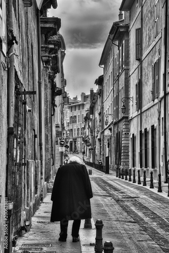Black and white vertical photo of a lone person on a small French street, neither the buildings nor the person are recognizable