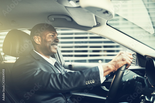 Smiling African businessman driving his car through the city str