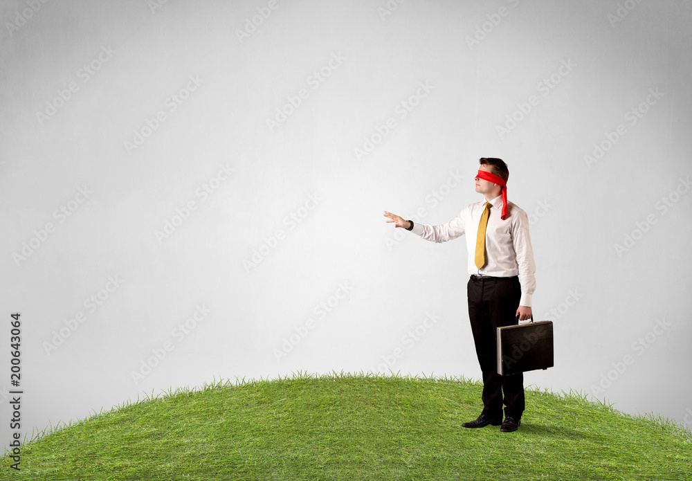 Young blindfolded businessman steps on a patch of grass Young blindfolded businessman steps on a patch of grass