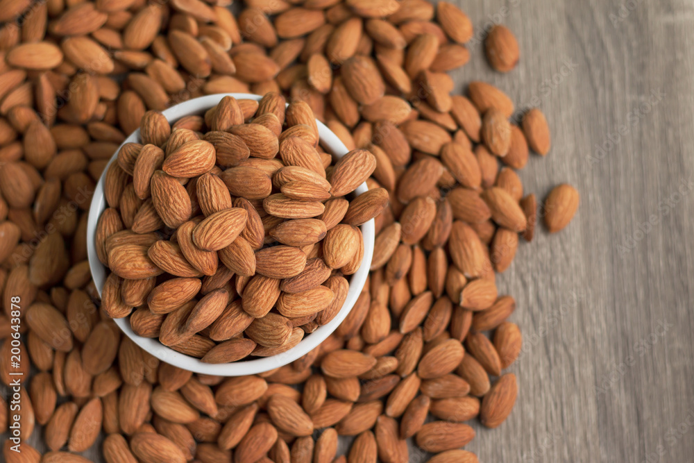 Pile of almonds nut in a while bowl against wooden background select focus shallow depth of field Pile of almonds nut in a while bowl against wooden background select focus shallow depth of field