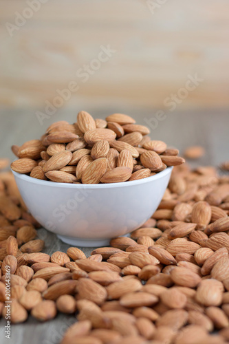 Pile of almonds nut in a while bowl against wooden background select focus shallow depth of fieldPile of almonds nut in a while bowl against wooden background select focus shallow depth of field