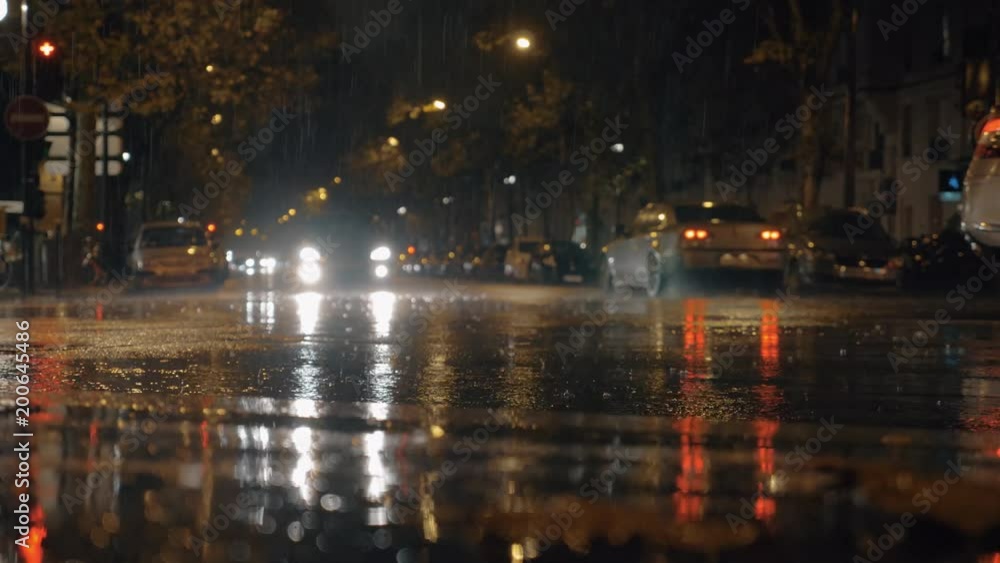 PARIS, FRANCE - SEPTEMBER 29, 2017: Slow motion shot of rain pouring in the street and making puddles, cars driving in night city PARIS, FRANCE - SEPTEMBER 29, 2017: Slow motion shot of rain pouring in the street and making puddles, cars driving in night city