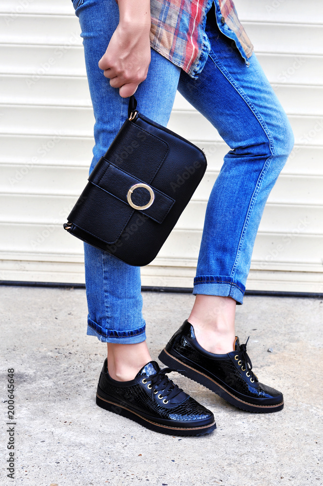 Fashion blogger outfit details. Street style fashion girl walking ,wearing  blue jeans black shoe lace shoes holding small handbag with details Stock  Photo | Adobe Stock