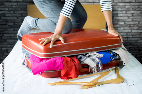 Travel and vacation concept, happiness woman packing stuff and a lot of clothes into suitcase on bed prepare for her travel and journey trip photo