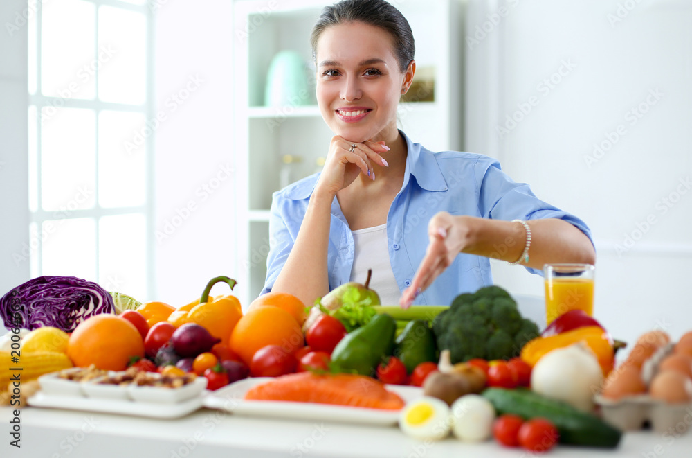 Young and cute woman sitting at the table full of fruits and vegetables in the wooden interior Young and cute woman sitting at the table full of fruits and vegetables in the wooden interior