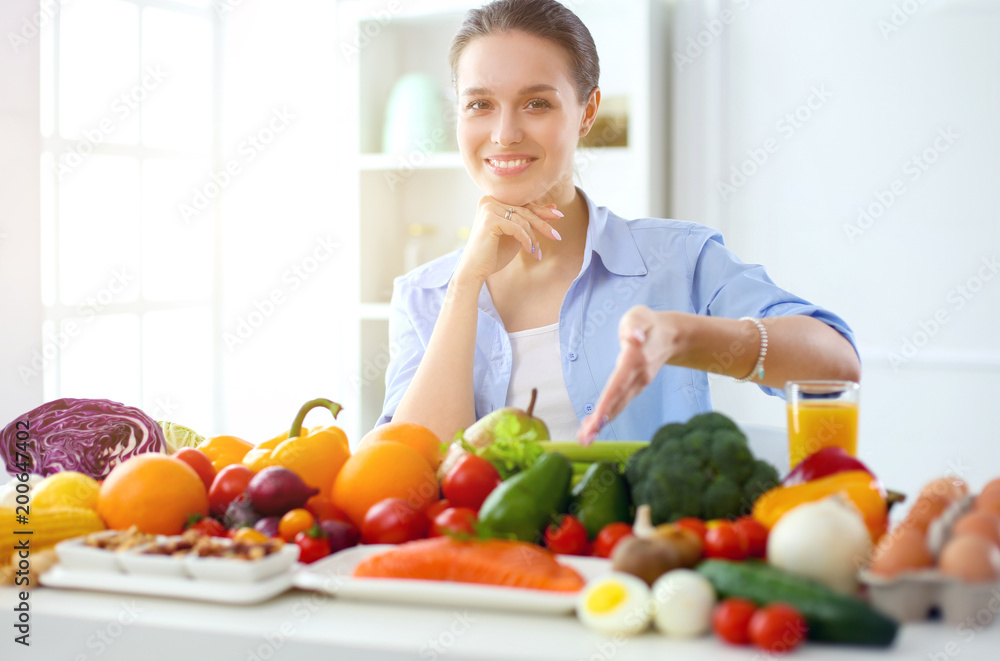 Young and cute woman sitting at the table full of fruits and vegetables in the wooden interior