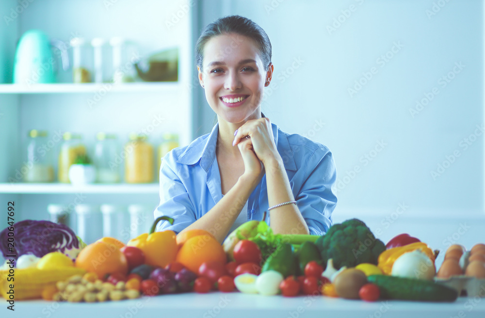 Young and cute woman sitting at the table full of fruits and vegetables in the wooden interior Young and cute woman sitting at the table full of fruits and vegetables in the wooden interior