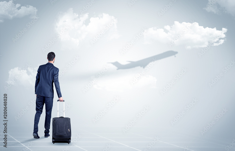 Young businessman with luggage walking towards an looking to a raising airplane
