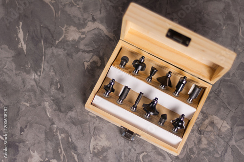 Set of steel router bit for milling cutter in rectangle wooden box with metal lock on old broken worn gray concrete floor with copy space